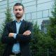 Businessman with arms crossed in front of modern office building, outdoors.